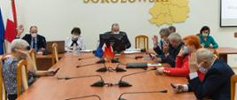 Na zdjęciu siedzący przy stole w Sali konferencyjnej Starostwa Powiatowego w Sokołowie Podlaskim radni Rady Powiatu Sokołowskiego głosują uchwałę poprzez podniesienie ręki. 