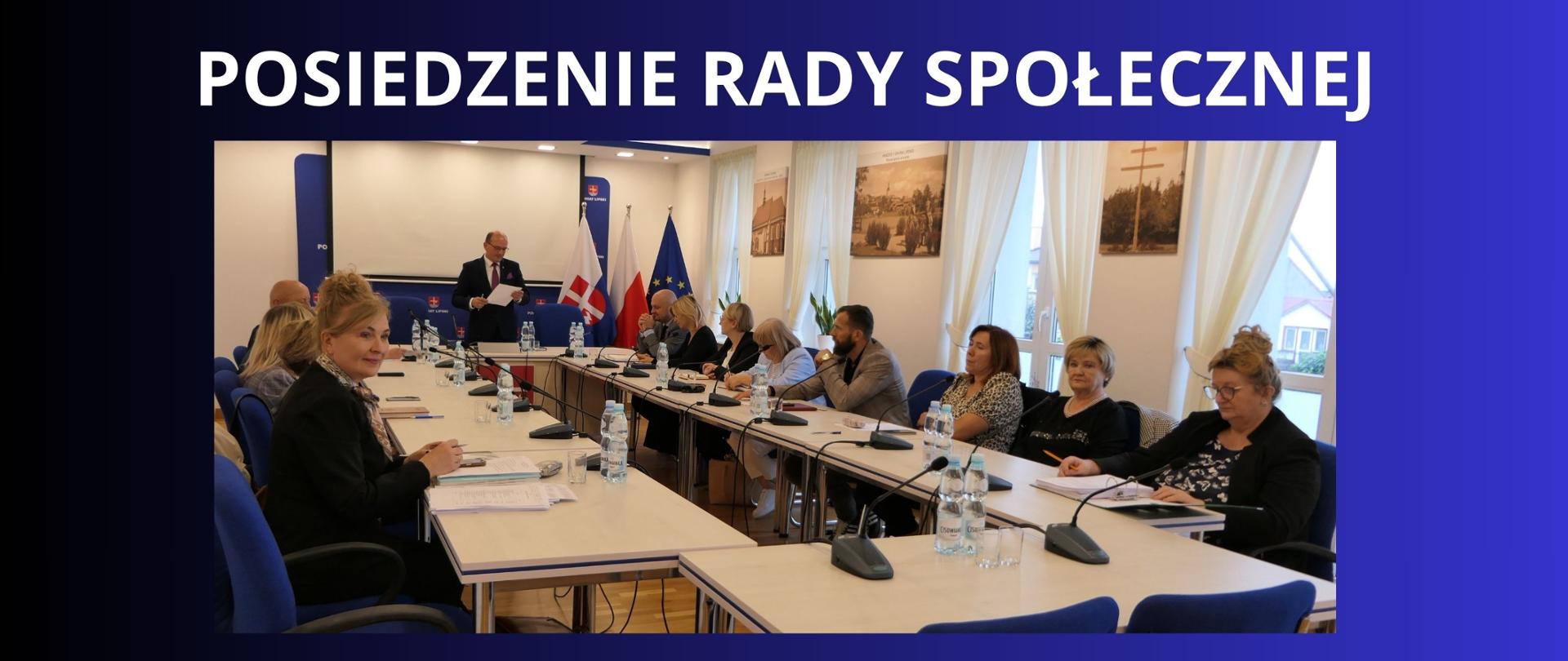 biały napis na granatowym tle" posiedzenie rady społecznej" zdjęcie z obrad rady , członkowie siedzą przy stołach na sali konferencyjnej Starostwa Powiatowego 