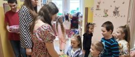 Przedstawiciele Samorządu Uczniowskiego rozdają dzieciom w szkole kolorowe czekoladowe jajeczka