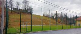 boisko do gry w piłkę, po prawej zabudowania, w oddali skarpa z nasadzeniami drzewek miododajnych