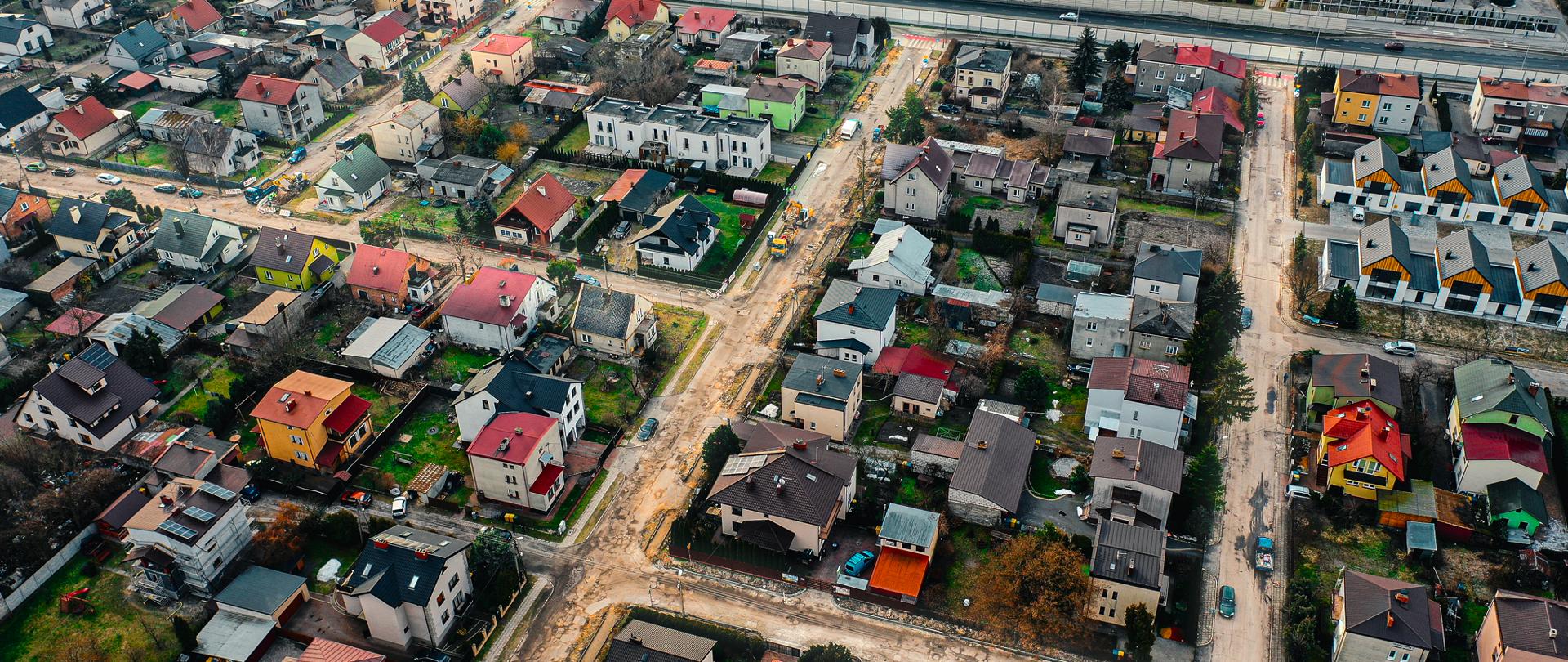 Zdjęcie przedstawia widok z drona na osiedle domków jednorodzinnych, na którym remontowane są drogi