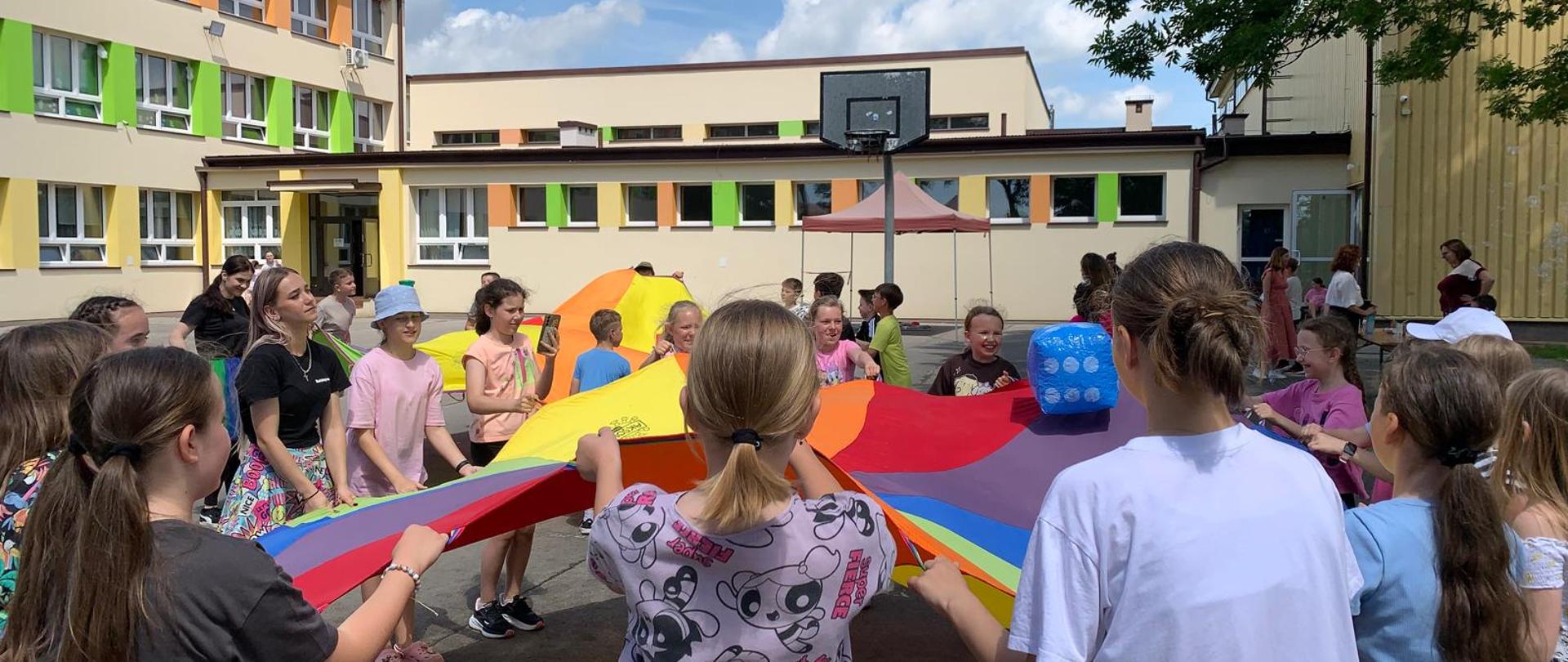 Dzieci bawią się z chustami animacyjnymi podczas szkolnego Dnia Dziecka.