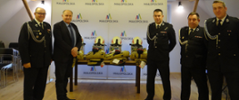 Zdjęcie przedstawia wójta gminy przekazującego zakupiono cztery komplety ubrania bojowego dla członków OSP Skawa.