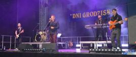 czterech mężczyzn na scenie trzech gra na instrumentach jeden śpiewa