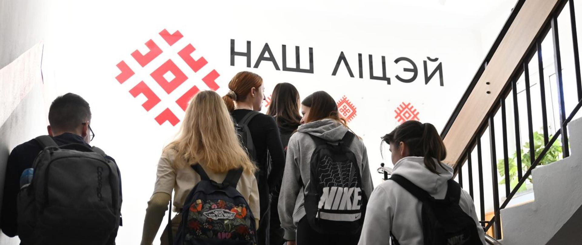 Uczniowie idą schodami na kolejne piętro, na ścianie napis w języku białoruskim "nasze liceum"