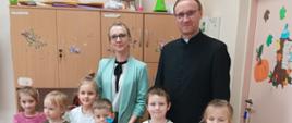 Nagrodzone w konkursie dzieci stoją w klasie, trzymają w ręku nagrody, za nimi od lewej Pani Dyrektor Szkoły i Ksiądz
