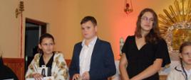 Trzy uczennice i jeden uczeń stoją przy ołtarzu, trzymają w rękach dyplomy i nagrody