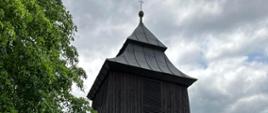 zdjęcie przedstawia drewnianą zabytkową dzwonnicę, która znajduje się obok Kościoła Parafialnego w Wietrzychowicach.