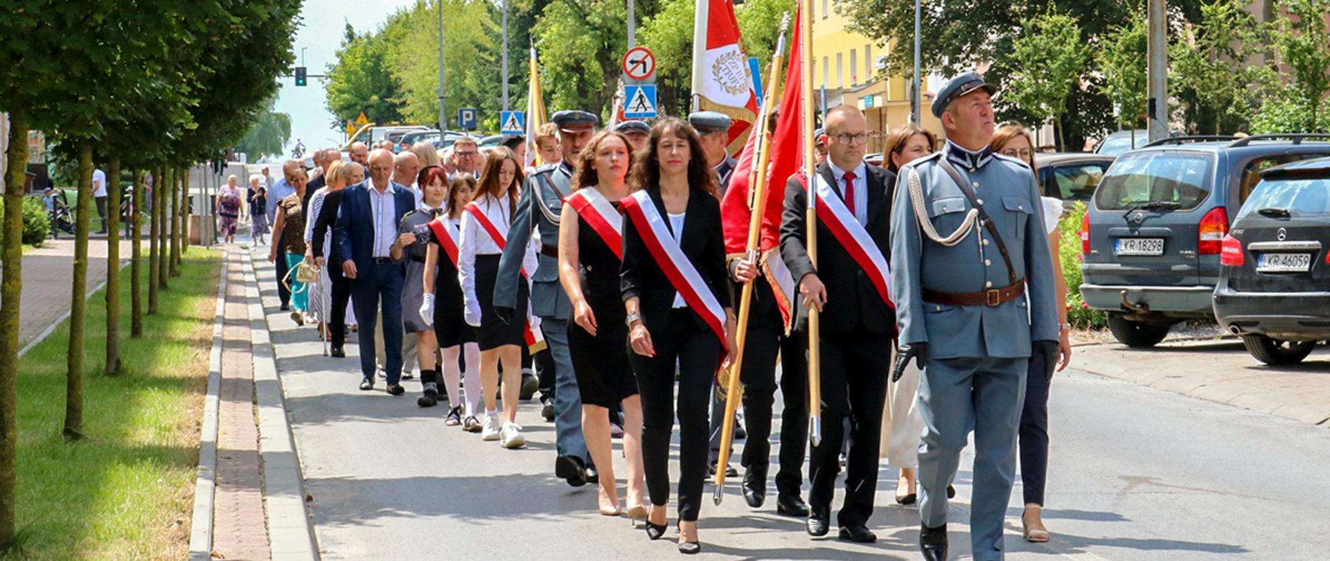 Zdjęcie przedstawia przemarsz uczestników wydarzenia ulicami miasta. Korowód prowadzony jest przez poczty sztandarowe.