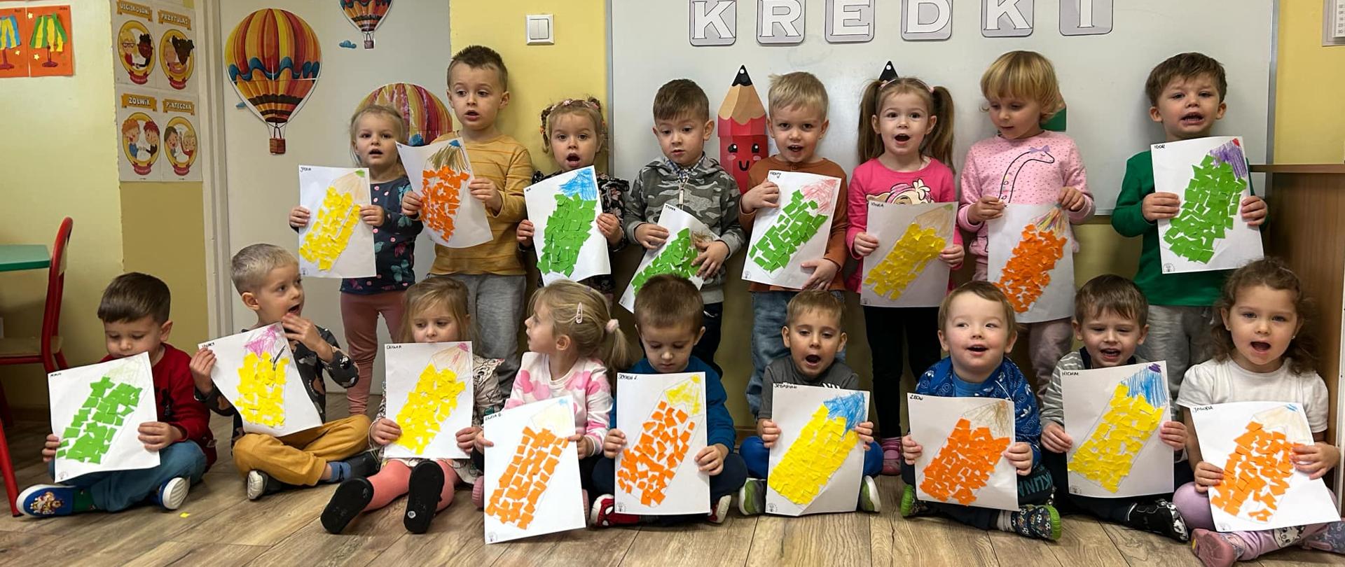 Dzieci w sali podczas zajęć prezentują pracę plastyczną wykonaną z okazji Dnia Kredki