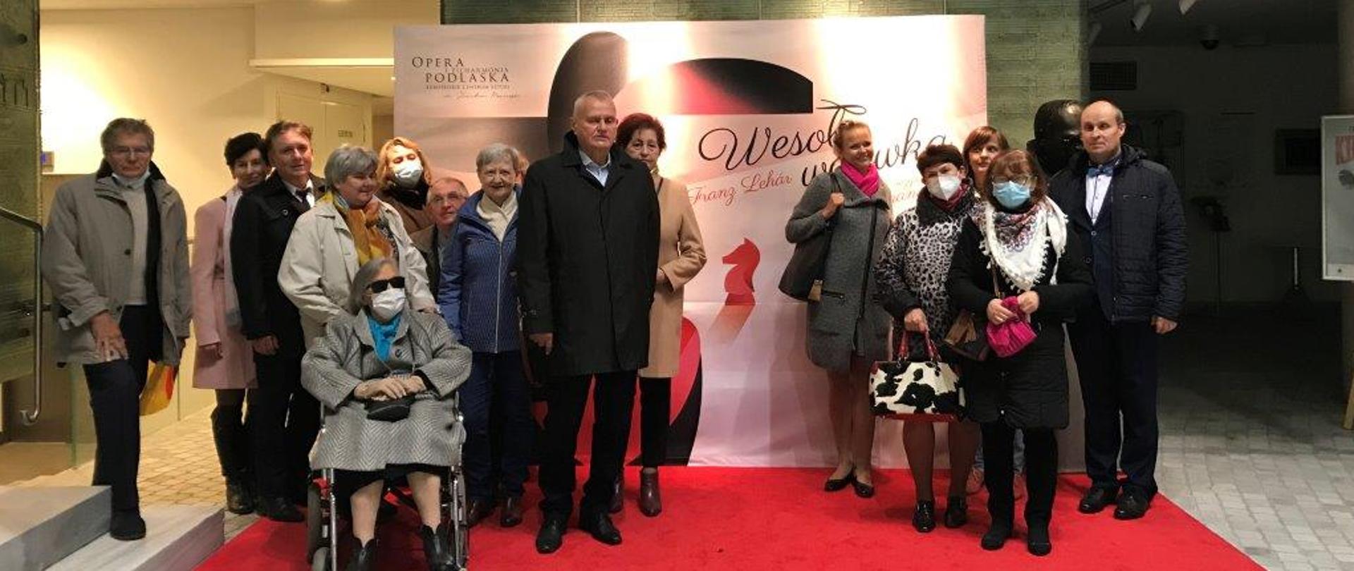 Członkowie Koła Niewidomych pozują przy banerze promującym spektakl w Operze