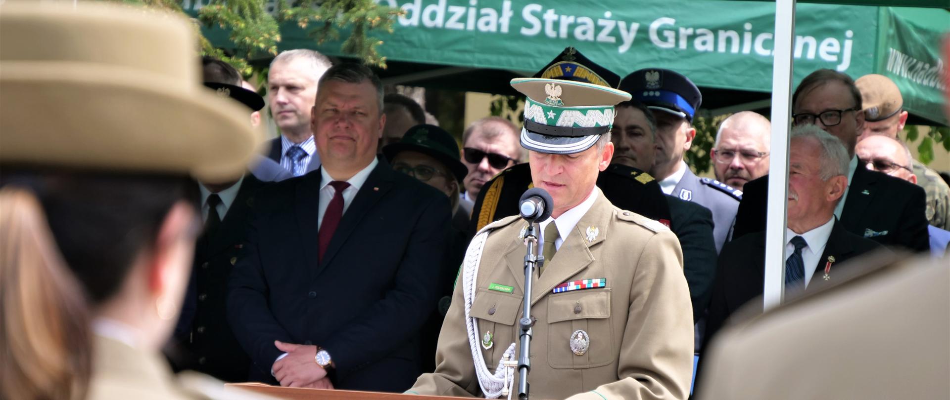 Zdjęcie przedstawia jedną osobę w mundurze stojącą przy mównicy i przemawiającą do mikrofonu