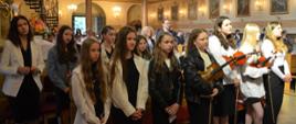 Schola w kościele w Rabie Wyżnej na mszy świętej z okazji Jubileusz 25-lecia nadania imienia Świętej Jadwigi Królowej. Dziewczyny w galowych strojach stoją w pierwszym rzędzie trzy z nich trzymają skrzypce. W tle widać sztandar szkoły oraz zaproszonych gości.