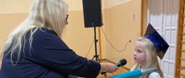 Pani dyrektor pasuje zielonym ołówkiem odświętnie ubranych uczniów klasy 1