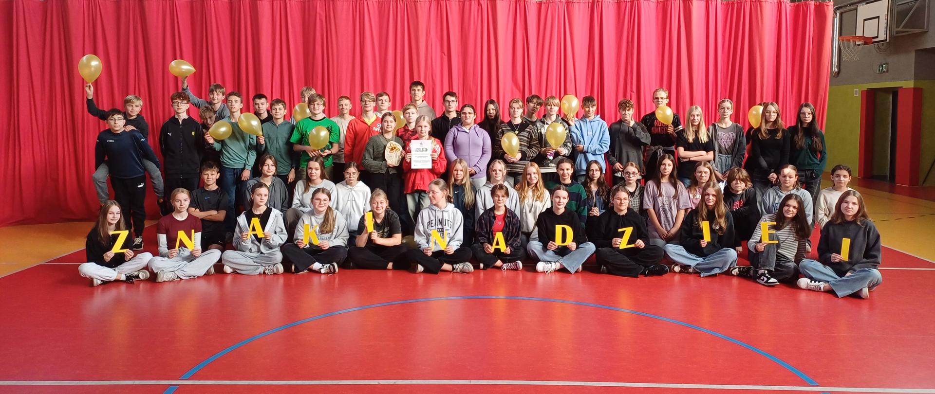 Duża grupa uczniów na tle czerwonej kotary