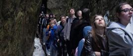 Uczestnicy wycieczki przechodzą wzdłuż wąwozu między skałami, podnoszą głowy do góry podziwiając wysokość skał