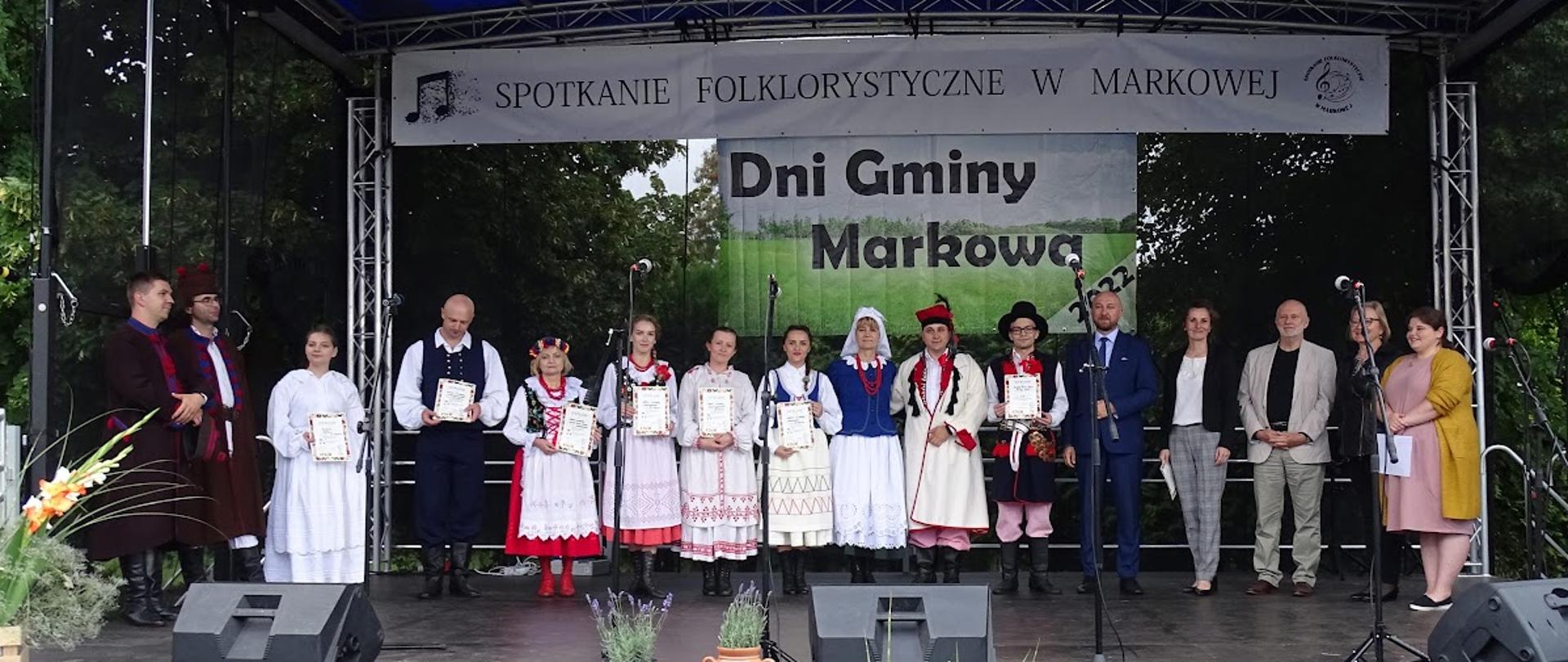 Zdjęcie przedstawia zespół ubrany w ludowe stroje pozujący do zdjęcia z dyplomami 