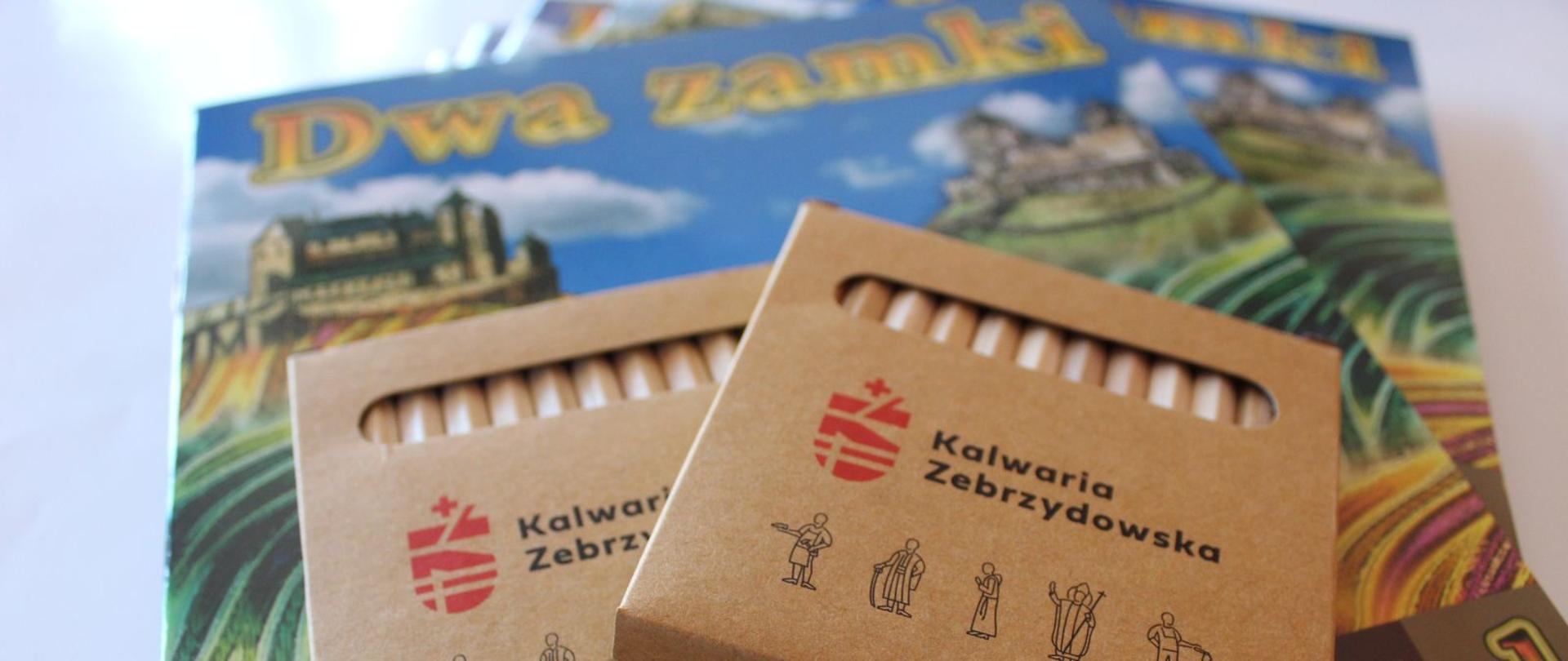Na pierwszym planie opakowanie kredek z logotypem Kalwarii Zebrzydowskiej, w tle kolorowanka "Dwa zamki"