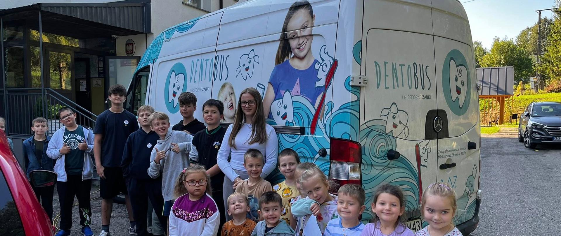 Uczniowie stoją przy Dentobusie, który jest zaparkowany przy szkole
