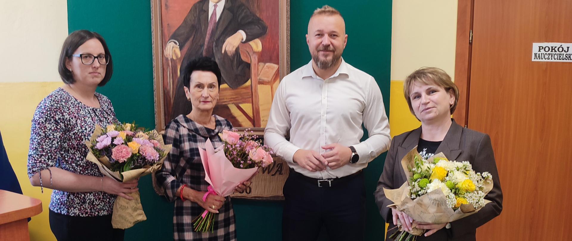 Trzy kobiety z bukietami kwiatów oraz mężczyzna w białej koszuli pozują do zdjęcia na tle zielonej sceny