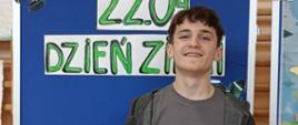 Uczeń nagrodzony w konkursie trzyma w ręku dyplom i papierową torbę z nagrodą