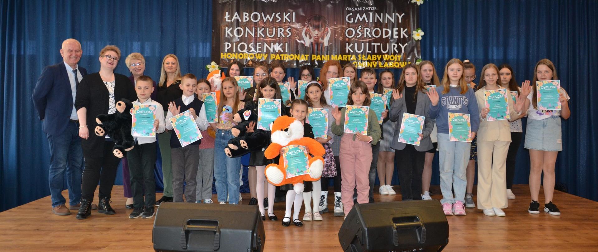 Uczestnicy i laureaci Łabowskiego Konkursu Piosenki stoją na scenie Gminnego Ośrodka Kultury w Łabowej z nagrodami i dyplomami