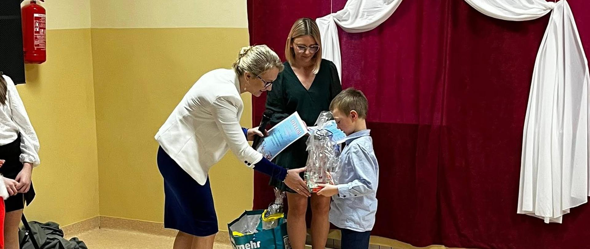 Pani dyrektor wraz z nauczycielką, która organizowała konkurs wręczają nagrodę uczniowi
