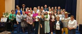 Zdjęcie przedstawia mieszkańców Gminy grodzisko Dolne ubranych odświętnie, stojących na scenie Ośrodka Kultury w Grodzisku Dolnym, uśmiechnięci