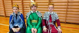 Trzech uczniów przebranych za trzech króli, od lewej uczeń w niebieskiej szacie w koronie na głowie, w środku uczeń w zielonej szacie z turbanem na głowie, po prawej uczeń w bordowej szacie z koroną na głowie