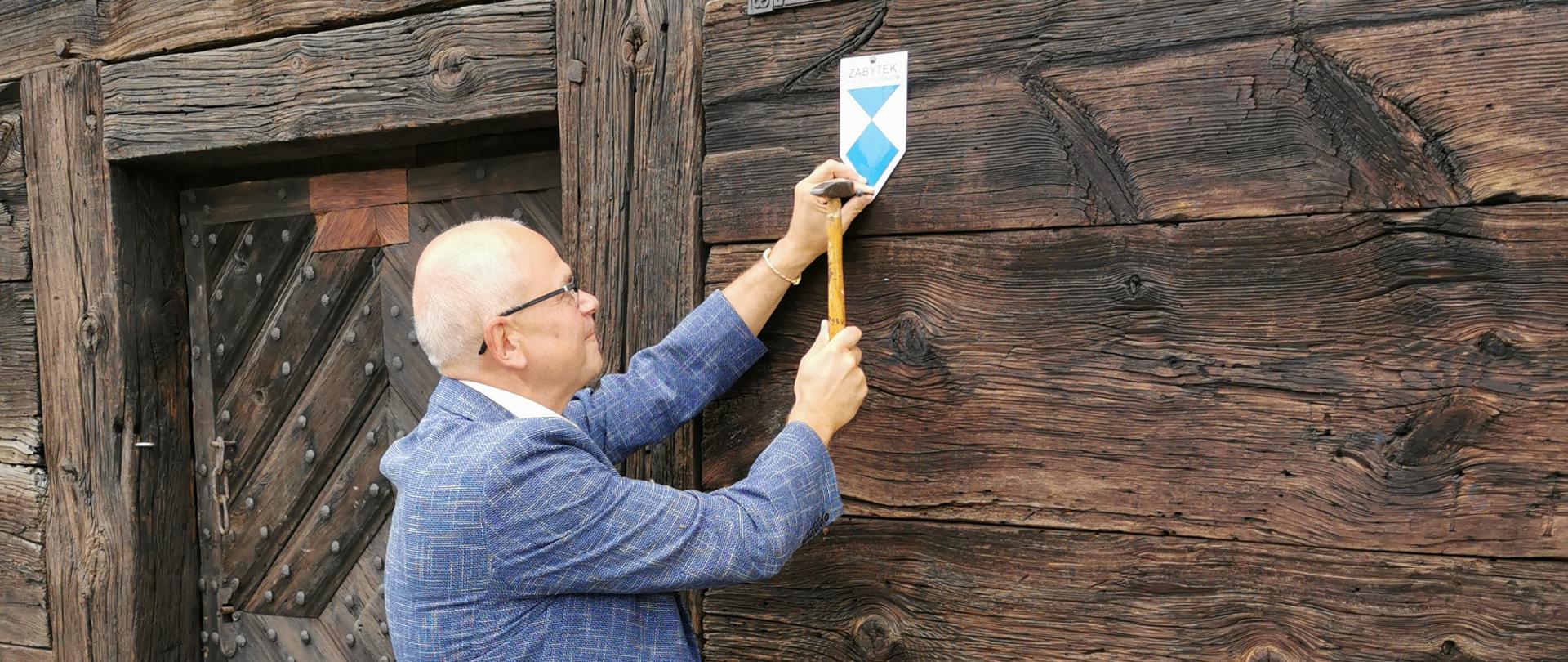 Burmistrz Jacek Gursz przybija tabliczkę "Zabytek chroniony prawem" na zabytkowym lamusie tkackim 