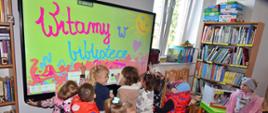 grupka dzieci z wizytą w bibliotece, rysują na tablicy interaktywnej