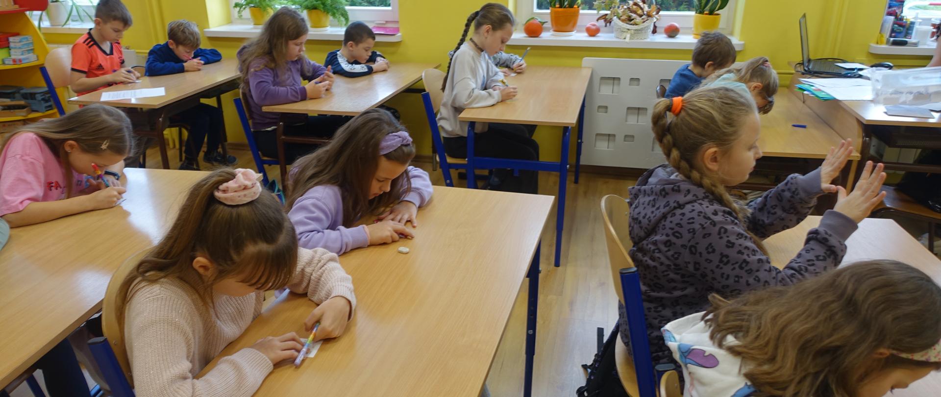 Uczniowie siedząc w ławkach zmagają się z tabliczką mnożenia