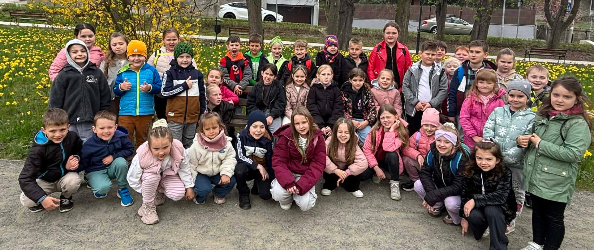 Grupa uśmiechniętych dzieci stoi w półkolu w parku.