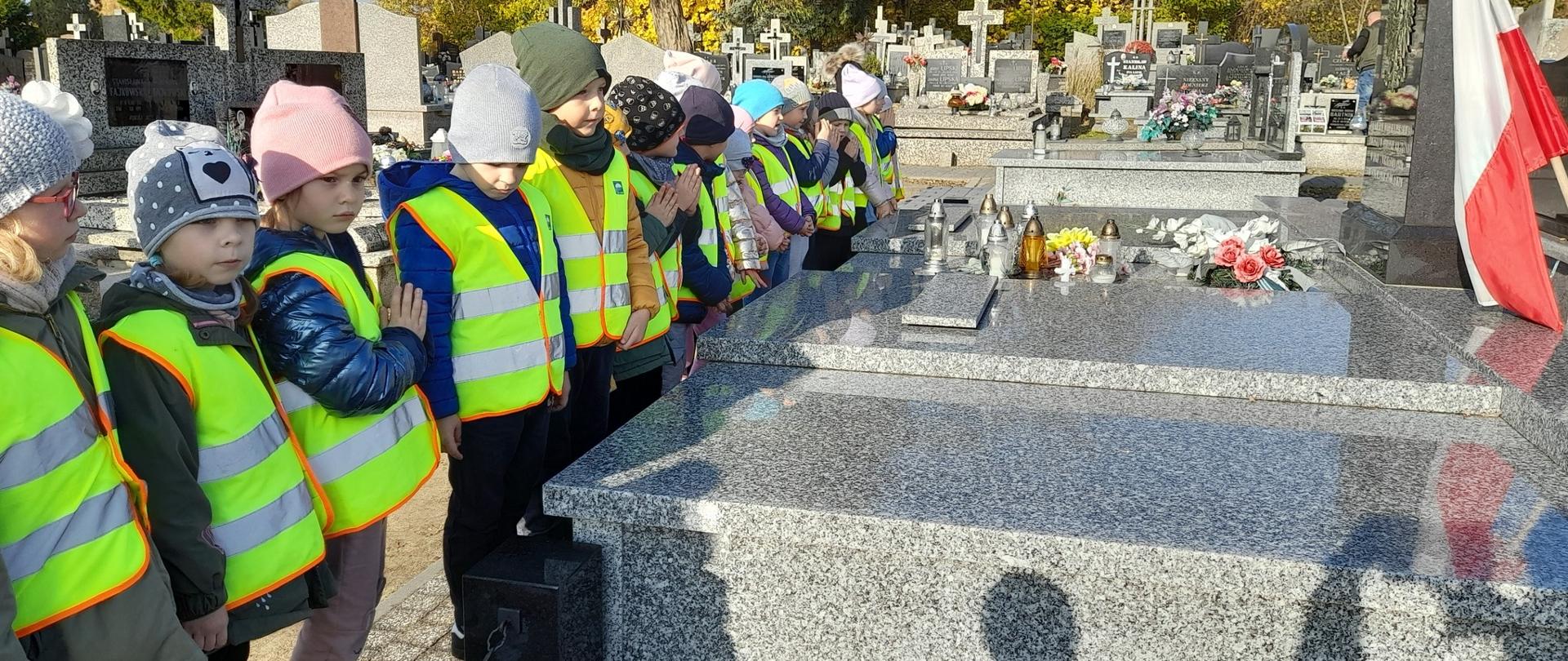 Dzieci w odblaskowych koszulkach stają przed grobem