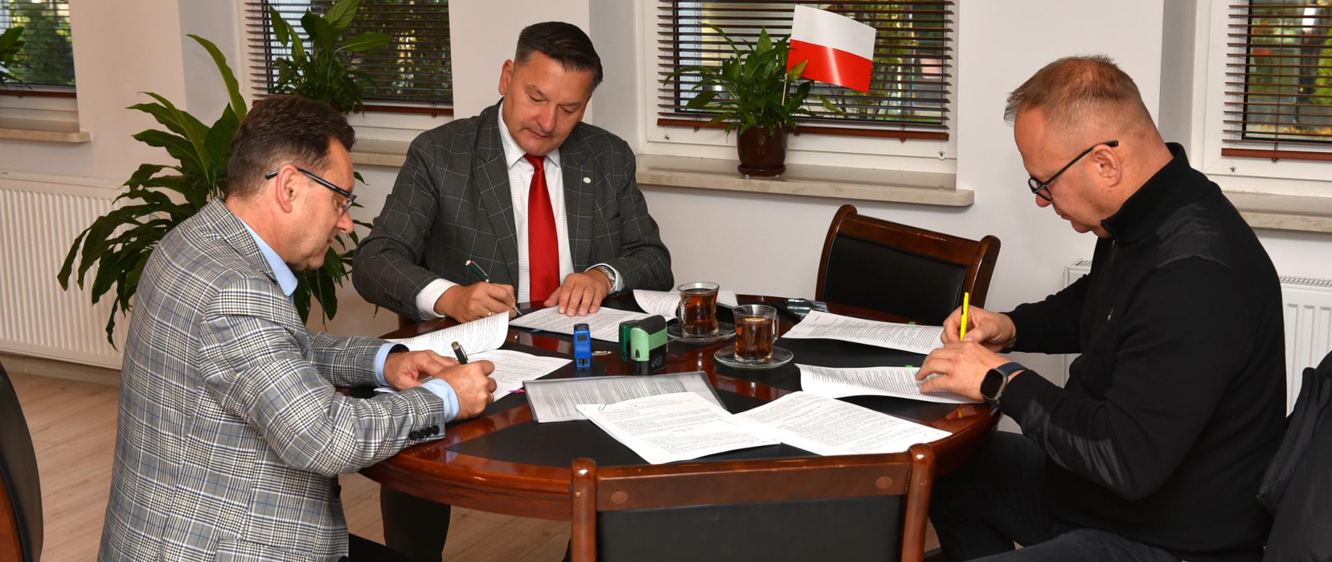 Na fotografii reprezentanci Powiatu Sokołowskiego wraz z wykonawcą podpisują umowy przy siedząc przy stole w gabinecie Starosty Sokołowskiego