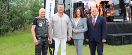 Na plenerowym wydarzeniu pod sceną pozuje grupa gości, wśród których znajduje się starosta zambrowska Edyta Marchelska-Groszfeld w eleganckim, szarym garniturze. Obok niej stoją m.in. motocyklista w skórzanym stroju oraz mężczyźni w oficjalnych i casualowych ubraniach. W tle widoczny jest telebim z hasłem „Rodzina Bogiem Silna”.