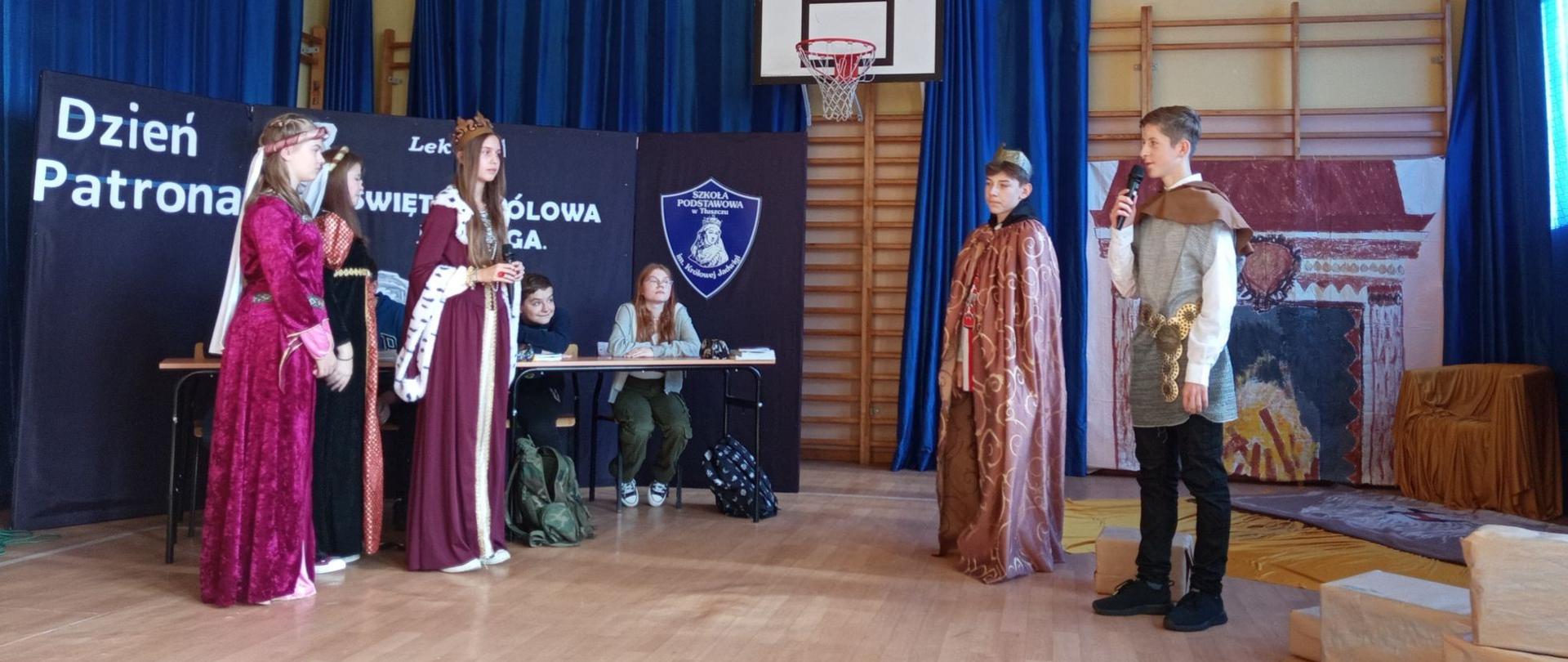 Dwie dziewczynki w długich sukniach, na przeciwko stoją dwaj chłopcy, jeden ubrany w długie szaty z koroną