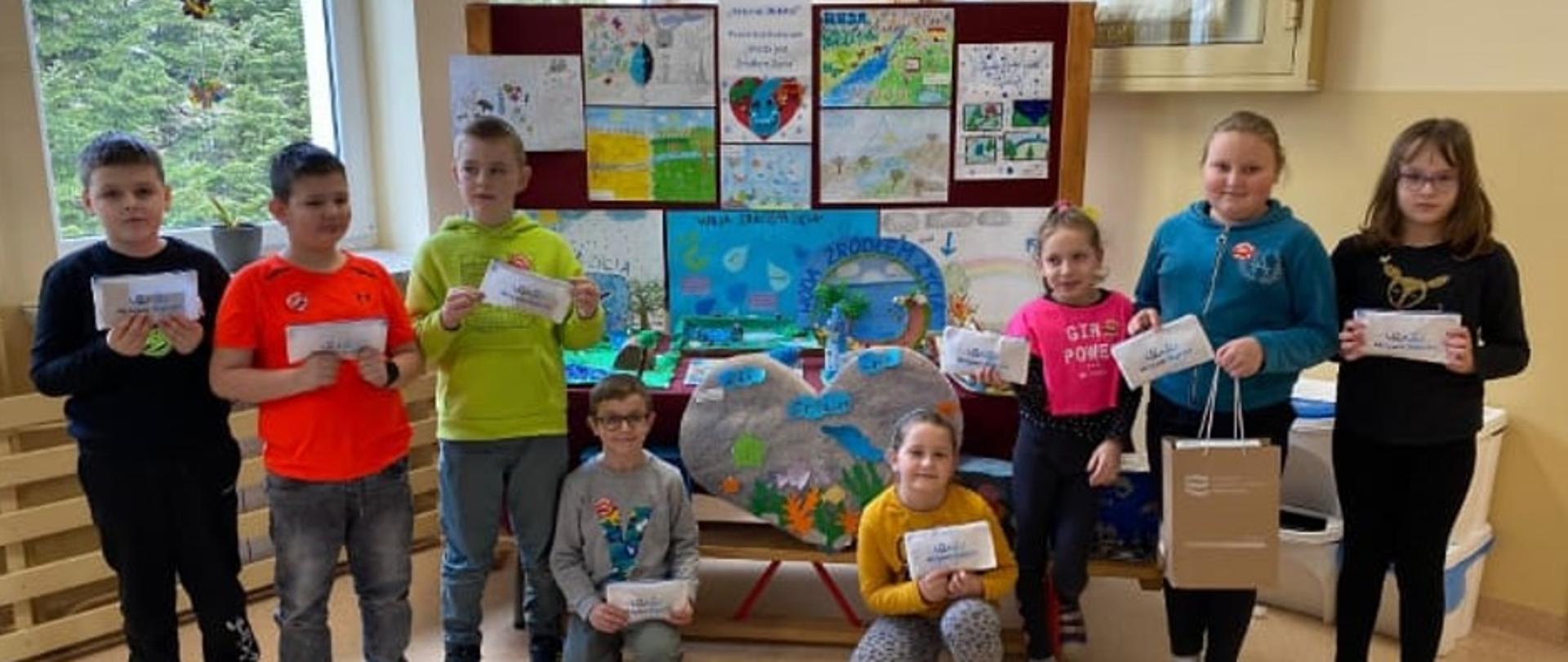 Nagodzeni uczniowie za prace plastyczne w ramach programu Aktywni Błękitni pozują do zdjęcia na tle swoich prac