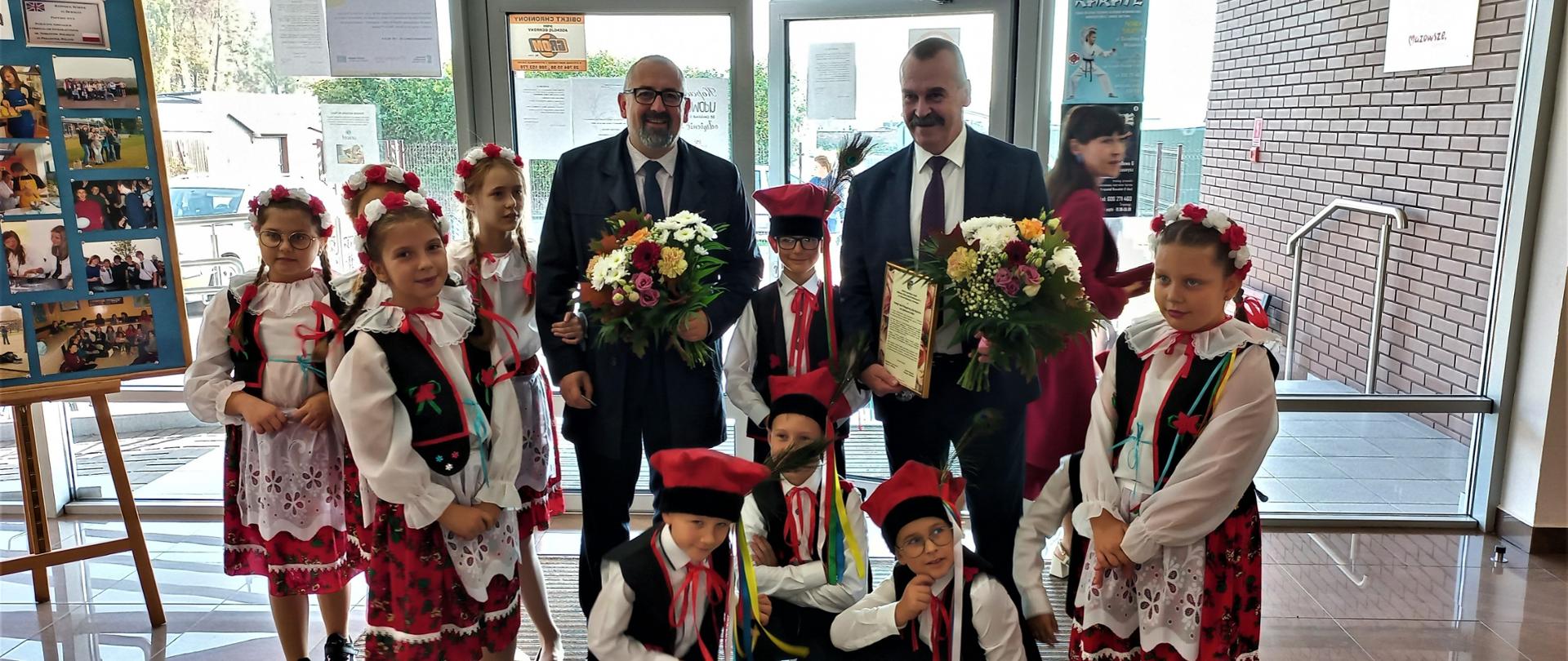 Na zdjęciu Starosta Krzysztof Bieńkowski oraz Wicestarosta Waldemar Trochimiuk w otoczeniu dzieci przebranych w stroje ludowe. 