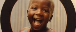 Śmiejące się dziecko. Wokół niego napis Miłego dnia, Redemptoris Missio Fundacja Pomocy Humanitarnej