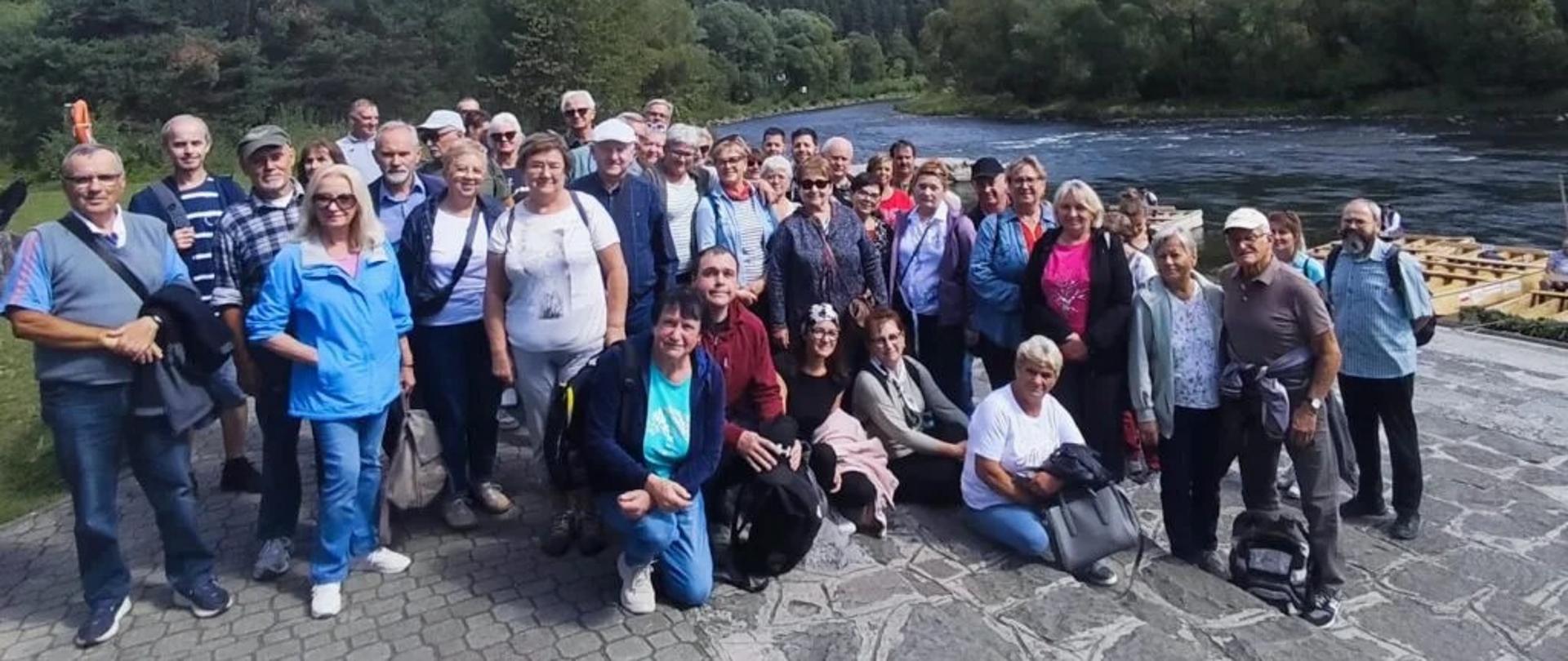 Grupa dorosłych osób pozuje do zdjęcia przy rzece, w tle góry