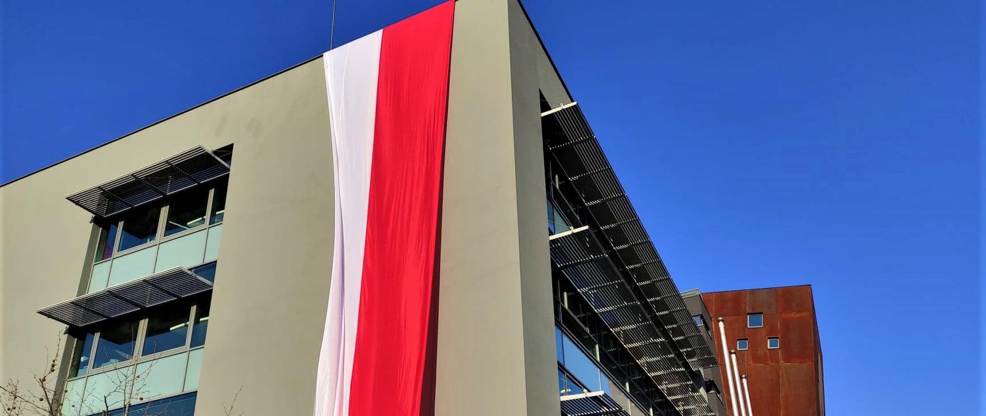 Biało-czerwona flaga zwisająca z budynku.