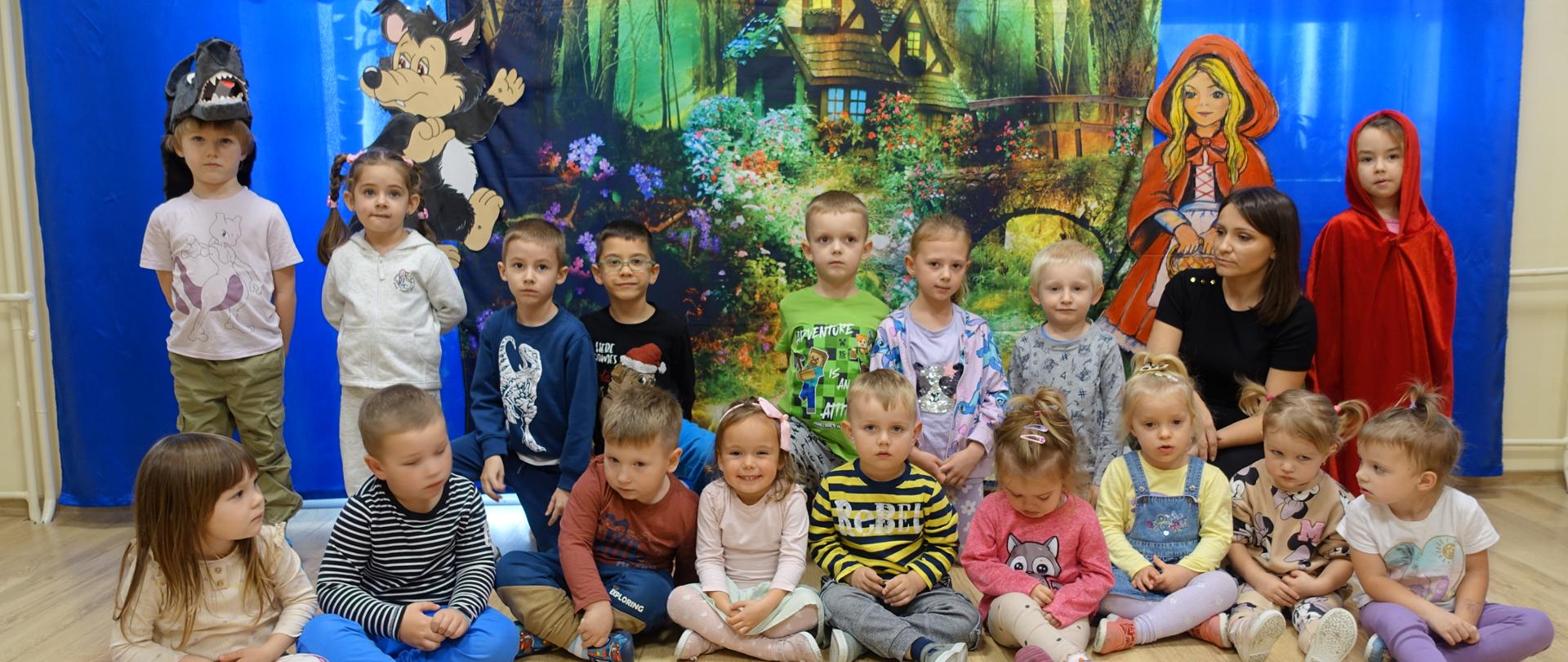Pamiątkowe zdjęcie dzieci z panią nauczycielką na tle baśniowej dekoracji