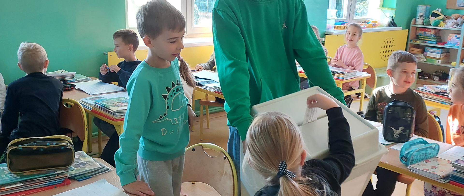 Głosowanie przez uczniów klasy II, uczeń klasy VIII zbiera głosy do urny.