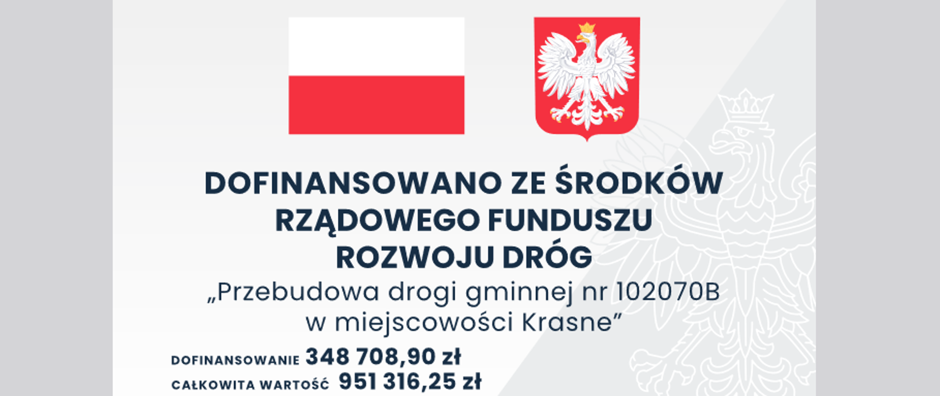Tablica w kolorze biało-szarym, znak wodny orła, na górze po lewej stronie flaga Polski, po prawej godło, niżej napis "Dofinansowano ze środków Rządowego Rozwoju Dróg", poniżej napis: Przebudowa drogi gminnej nr 102070B w miejscowości Krasne. Całkowita wartość 951 316,25 zł, wysokość dofinansowania zadania to: 348 708,90 zł.