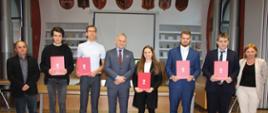 Grupa osób z czerwonymi teczkami w rękach pozuje do zdjęcia ze Starostą Polkowickim podczas uroczystości 