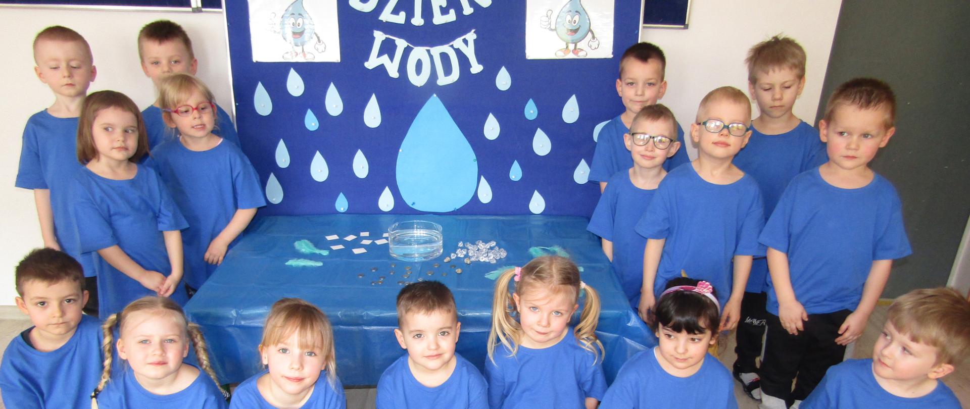 Dzieci w niebieskich koszulkach i tablica z kropelkami wody