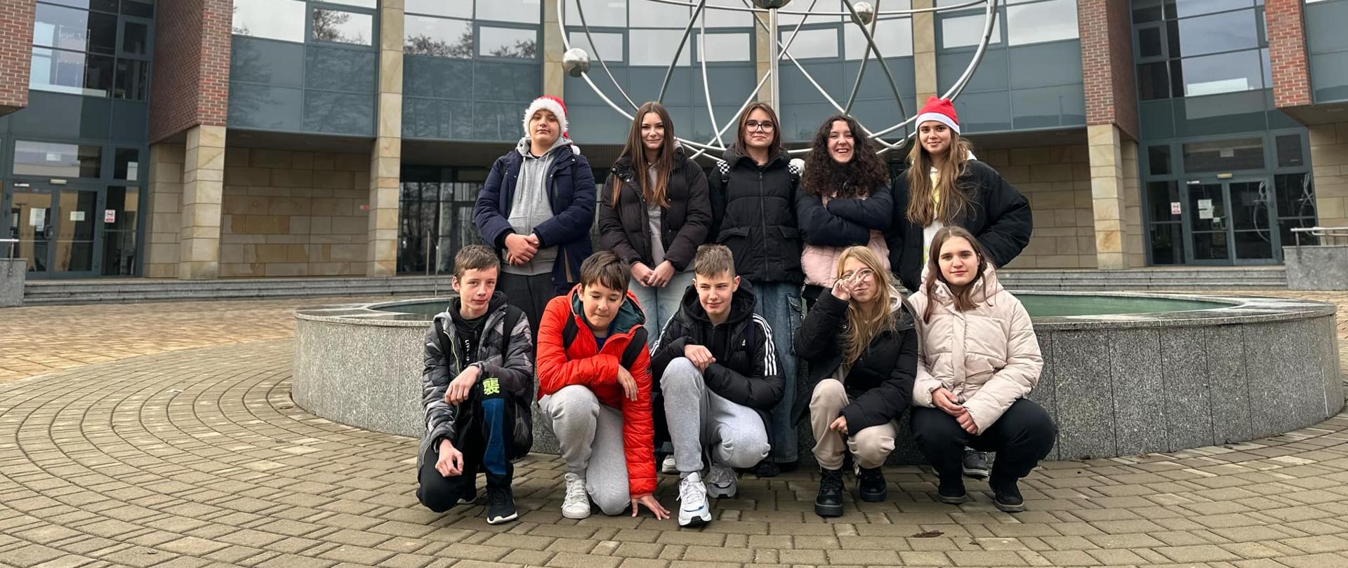 Grupka dziesięciu uczniów pozuje do zdjęcia przed budynkiem Wydziału Fizyki Astronomii i Informatyki Stosowanej Uniwersytetu Jagiellońskiego.