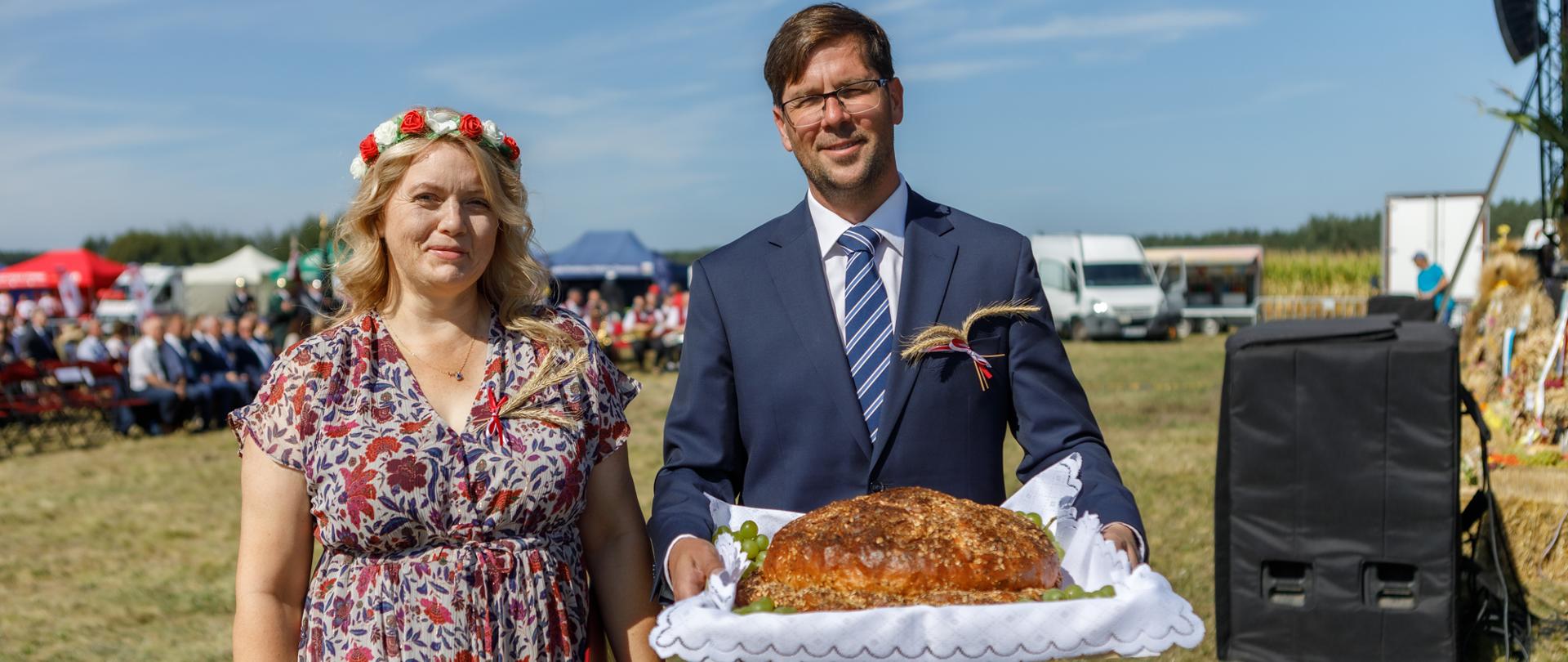 Mężczyzna i kobieta stoją obok siebie, mężczyzna trzyma chleb dożynkowy