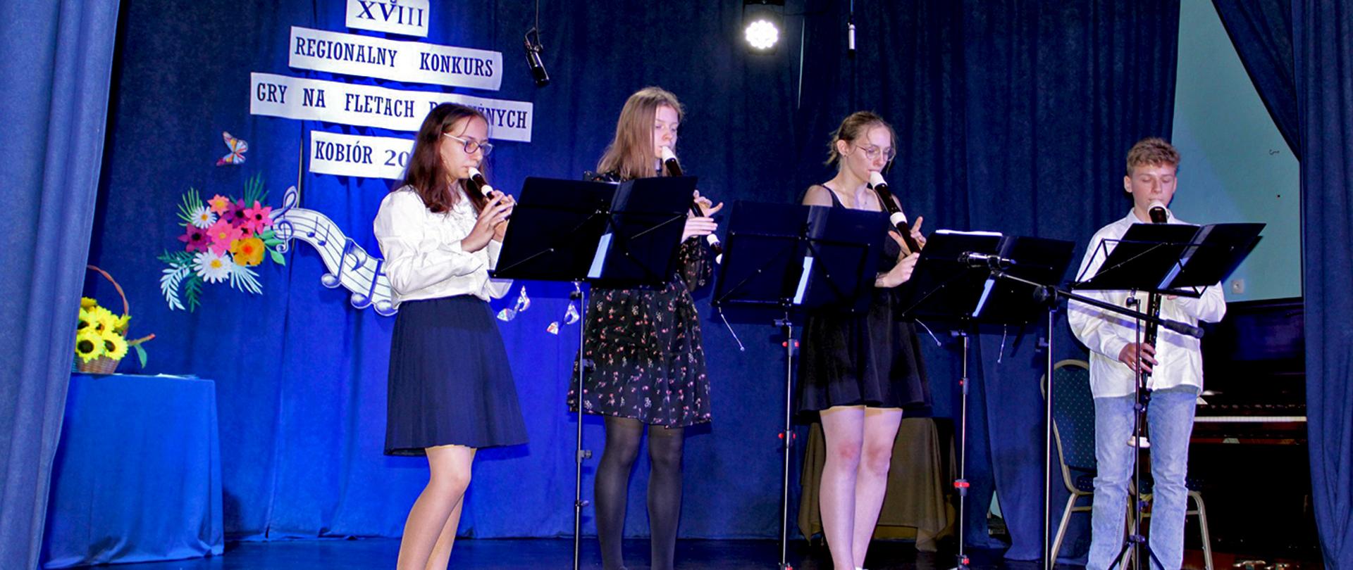 Czworo uczniów grających na fletach w tle niebieskie tło oraz napis Regionalny Konkurs Gry na Fletach Podłużnych